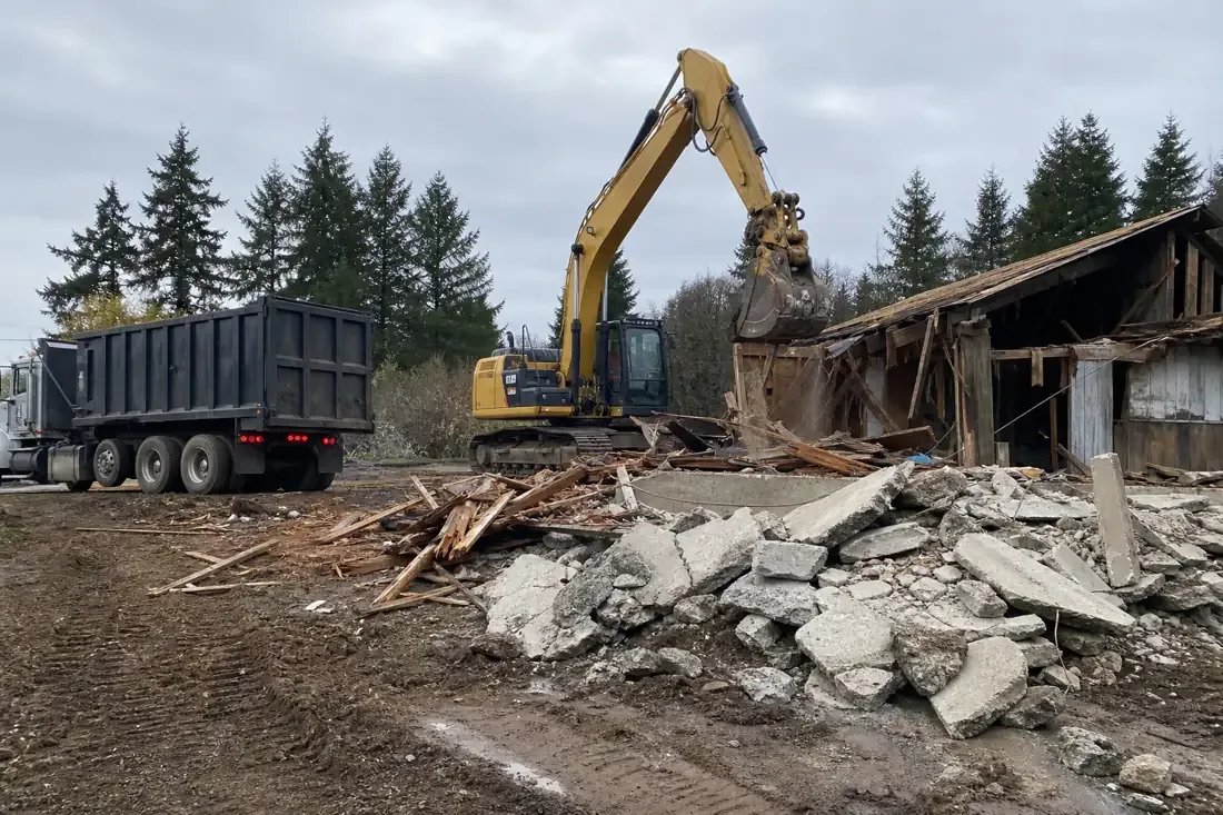 Excavator demolishing an old structure with a concrete and lumber debris pile in Beaverton, OR