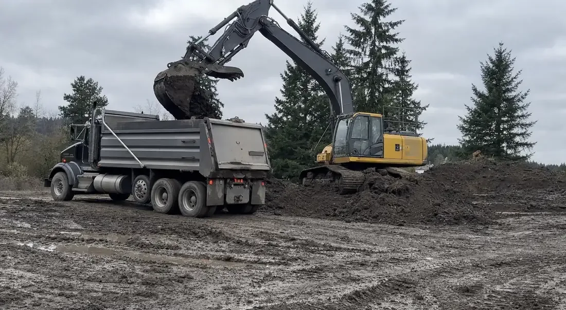 Dump truck being loaded with soil by an excavator for dirt hauling in Beaverton, OR